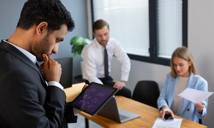 A businessman analyzing financial data and growth charts on a digital tablet while colleagues work in the background at WorthLift.
