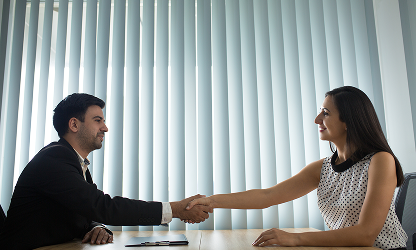A male executive and a female professional shaking hands across a conference table during a successful business meeting at WorthLift.